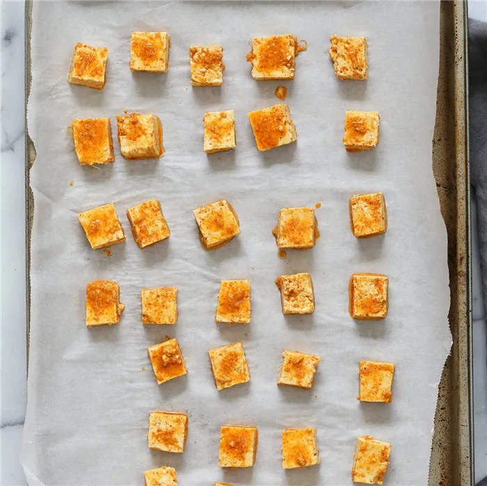 Marinated Tofu cubes on Parchment lined baking sheet ready to be baked for Indian Butter Tofu